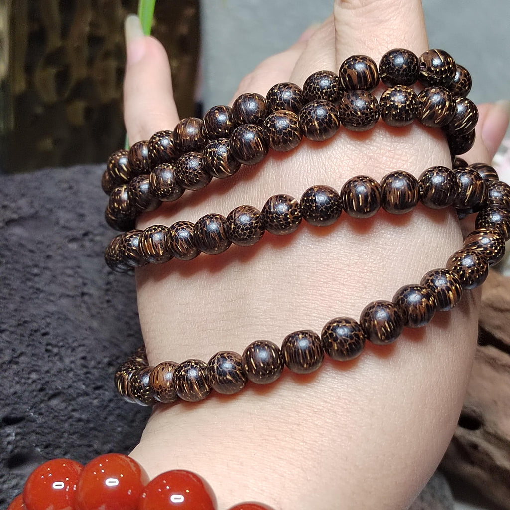 Close-up of a hand wearing two brown beaded bracelets on a blurred background