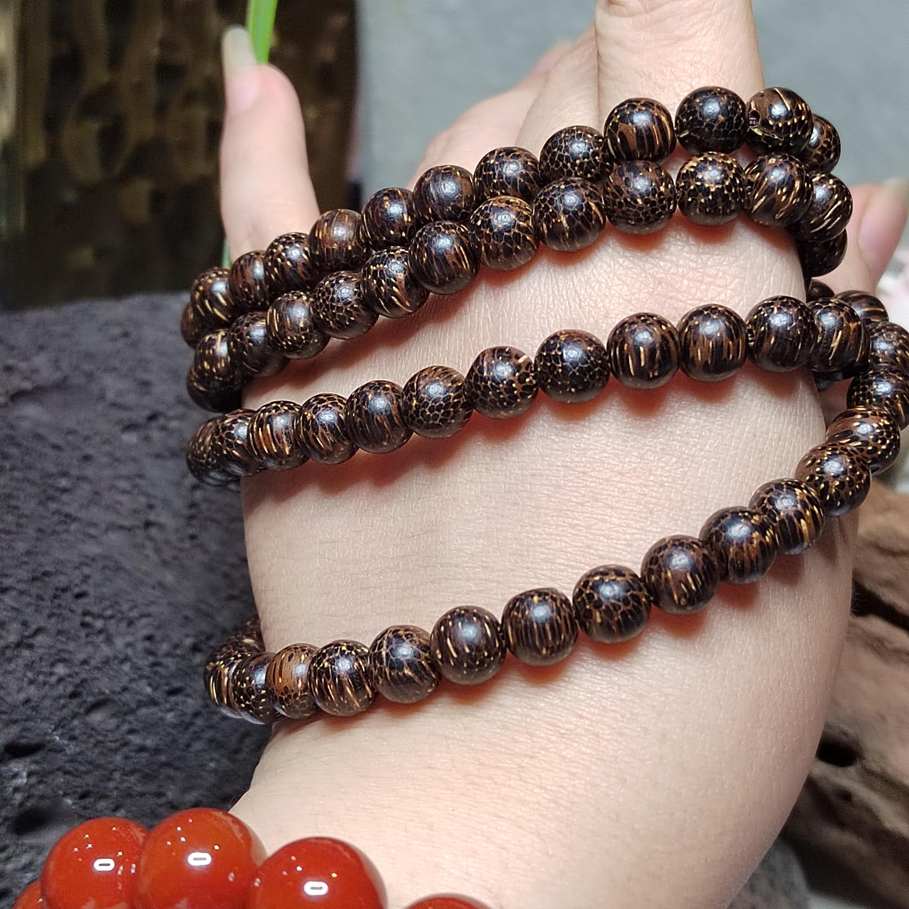 Close-up of a hand wearing two brown beaded bracelets on a blurred background