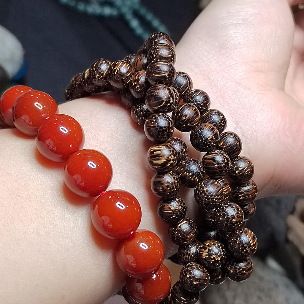 Close-up of a wrist wearing two bracelets, one with red beads and the other with brown beaded design.