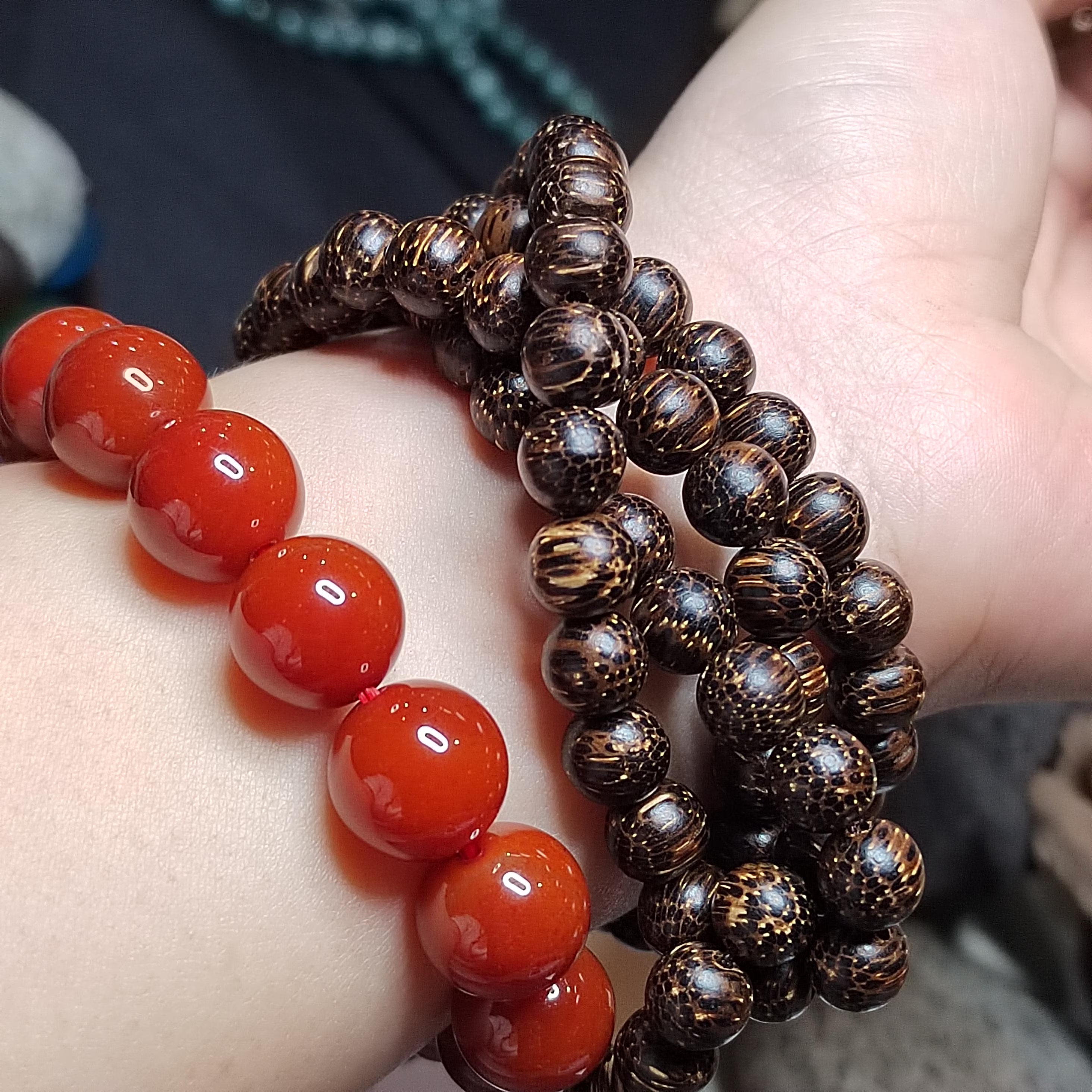 Close-up of a wrist wearing two bracelets, one with red beads and the other with brown beaded design.