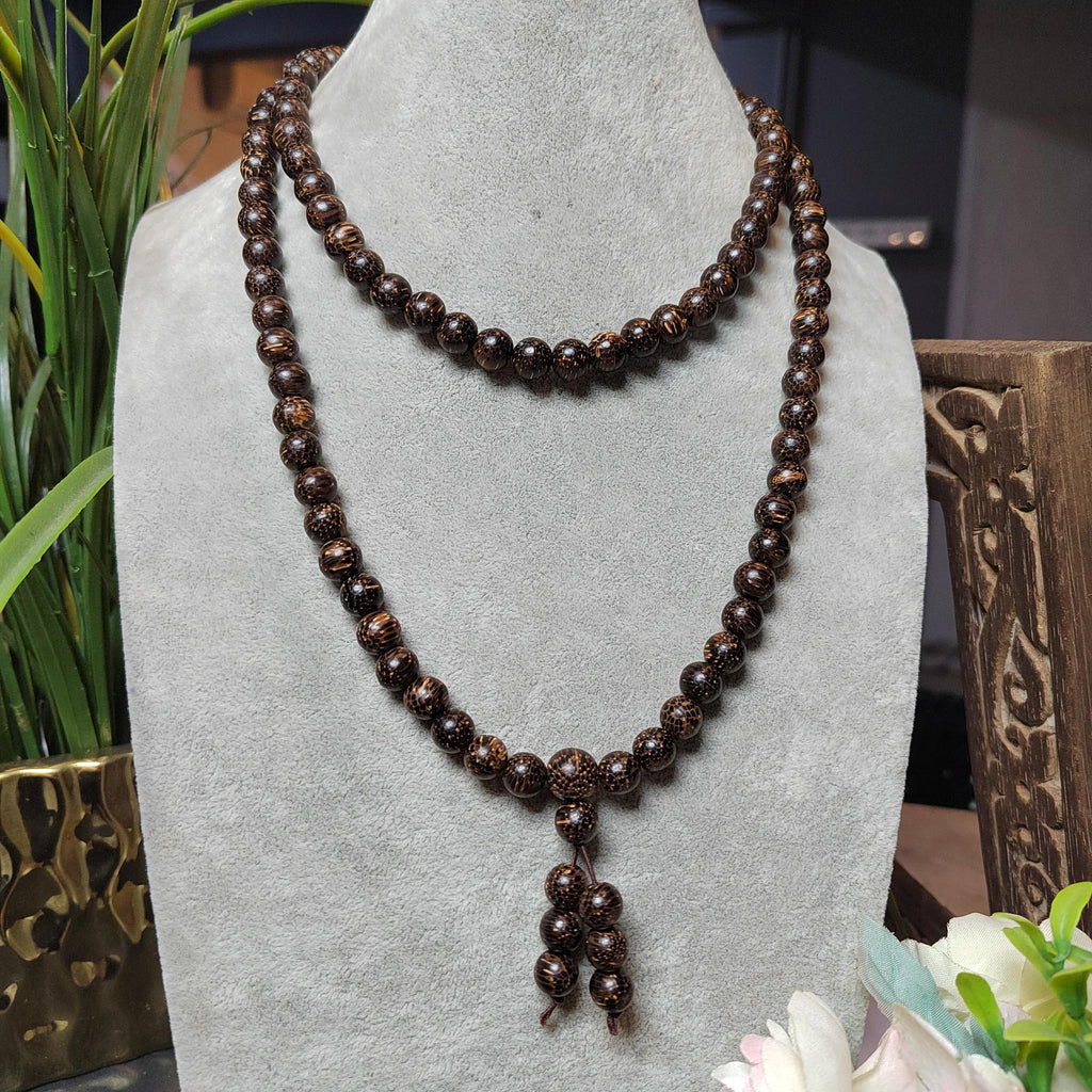 Brown beaded necklace on a gray stand with decorative elements in the background
