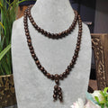 Brown beaded necklace on a gray stand with decorative elements in the background