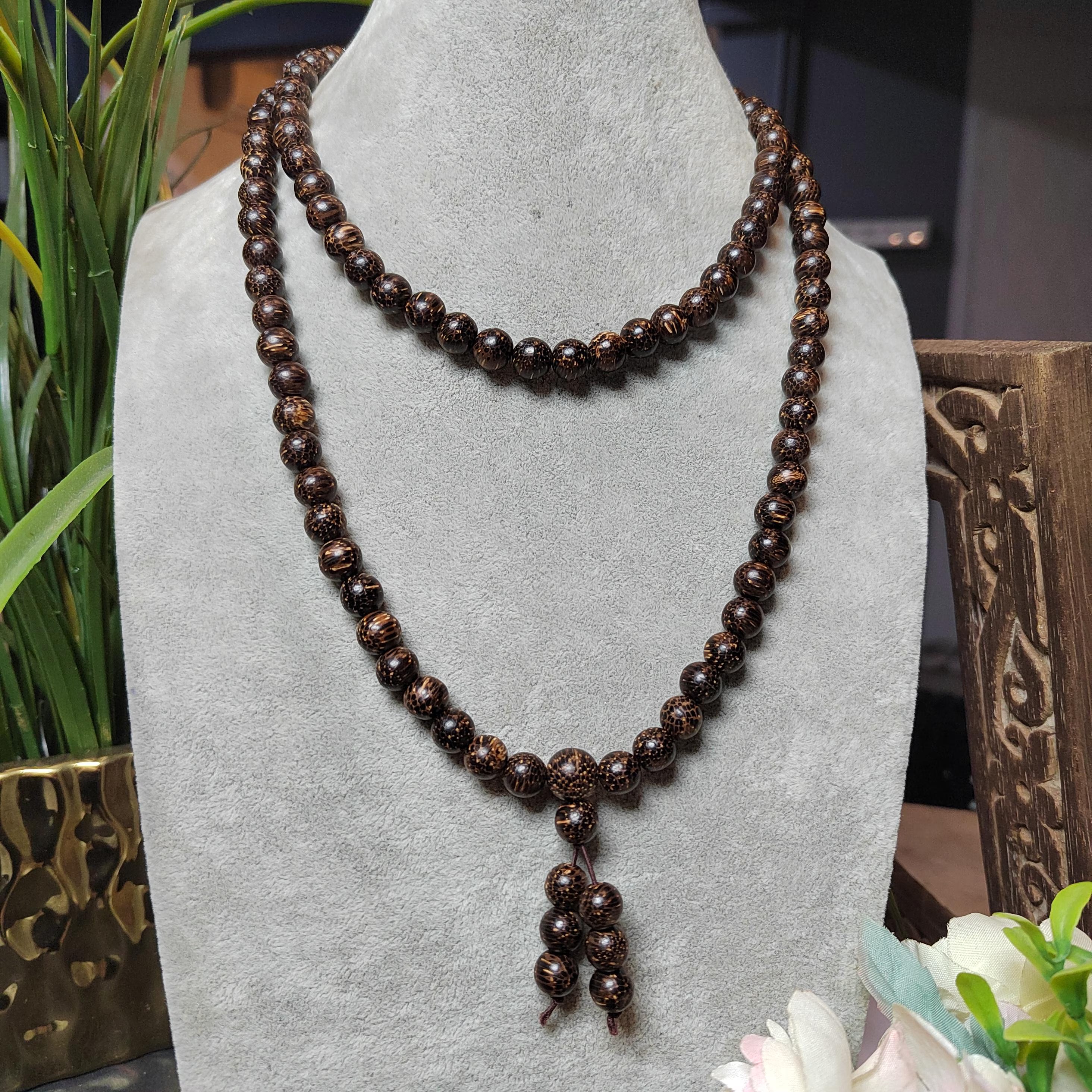 Brown beaded necklace on a gray stand with decorative elements in the background