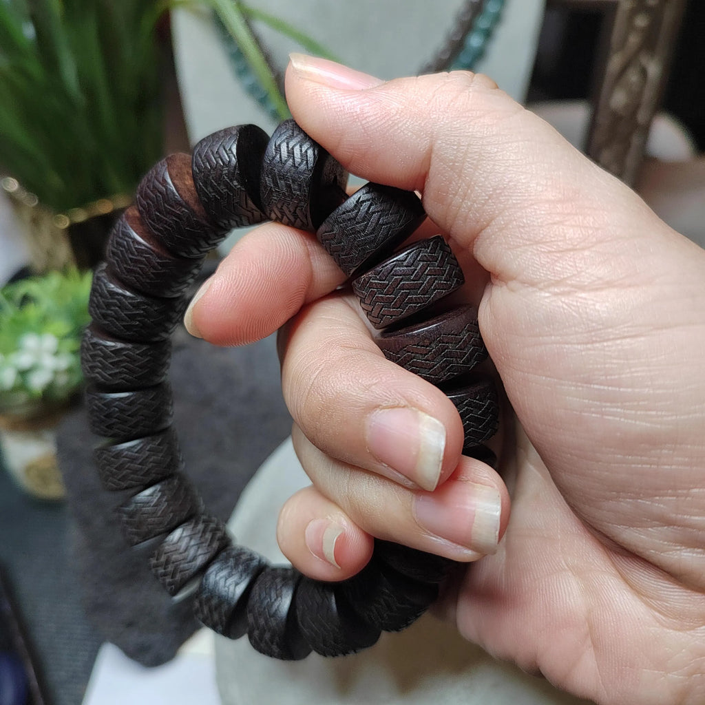 Hand holding a dark brown textured bracelet with a blurred indoor background