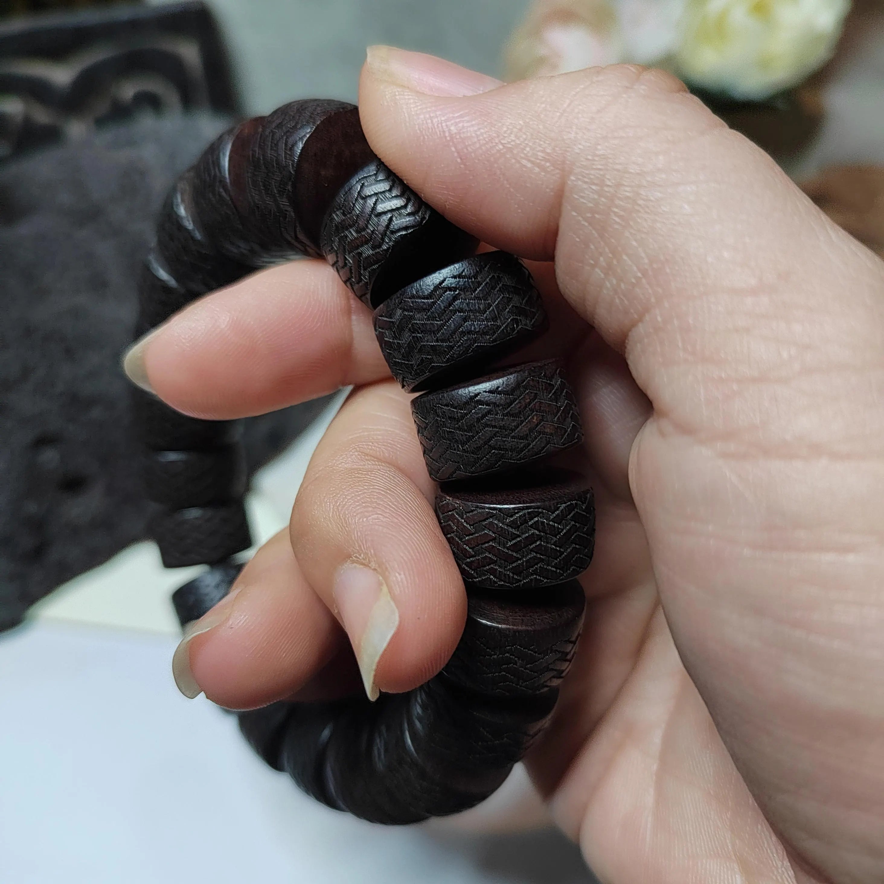 Hand holding a dark brown textured bracelet against a blurred background