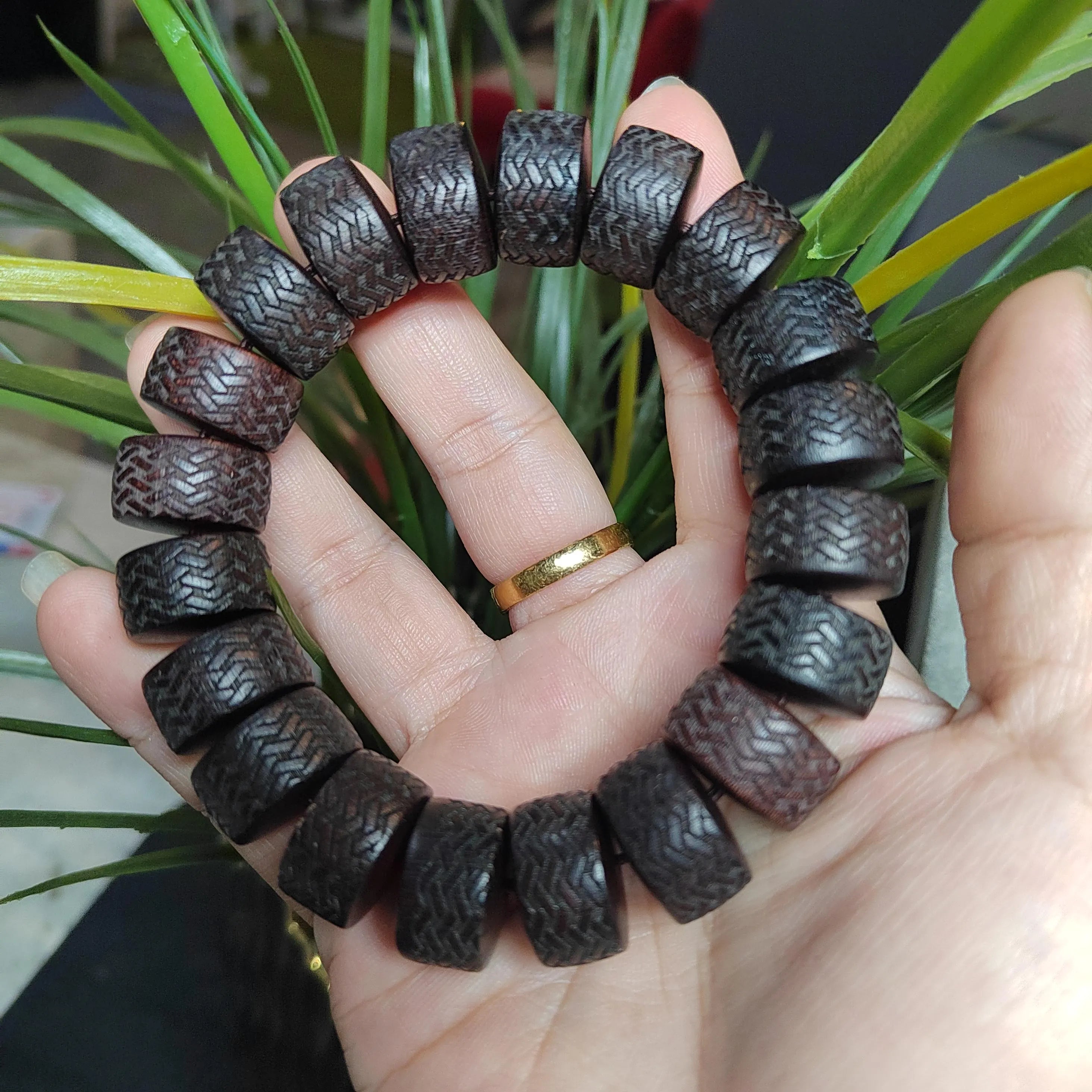 Hand holding a dark brown beaded bracelet with a plant in the background