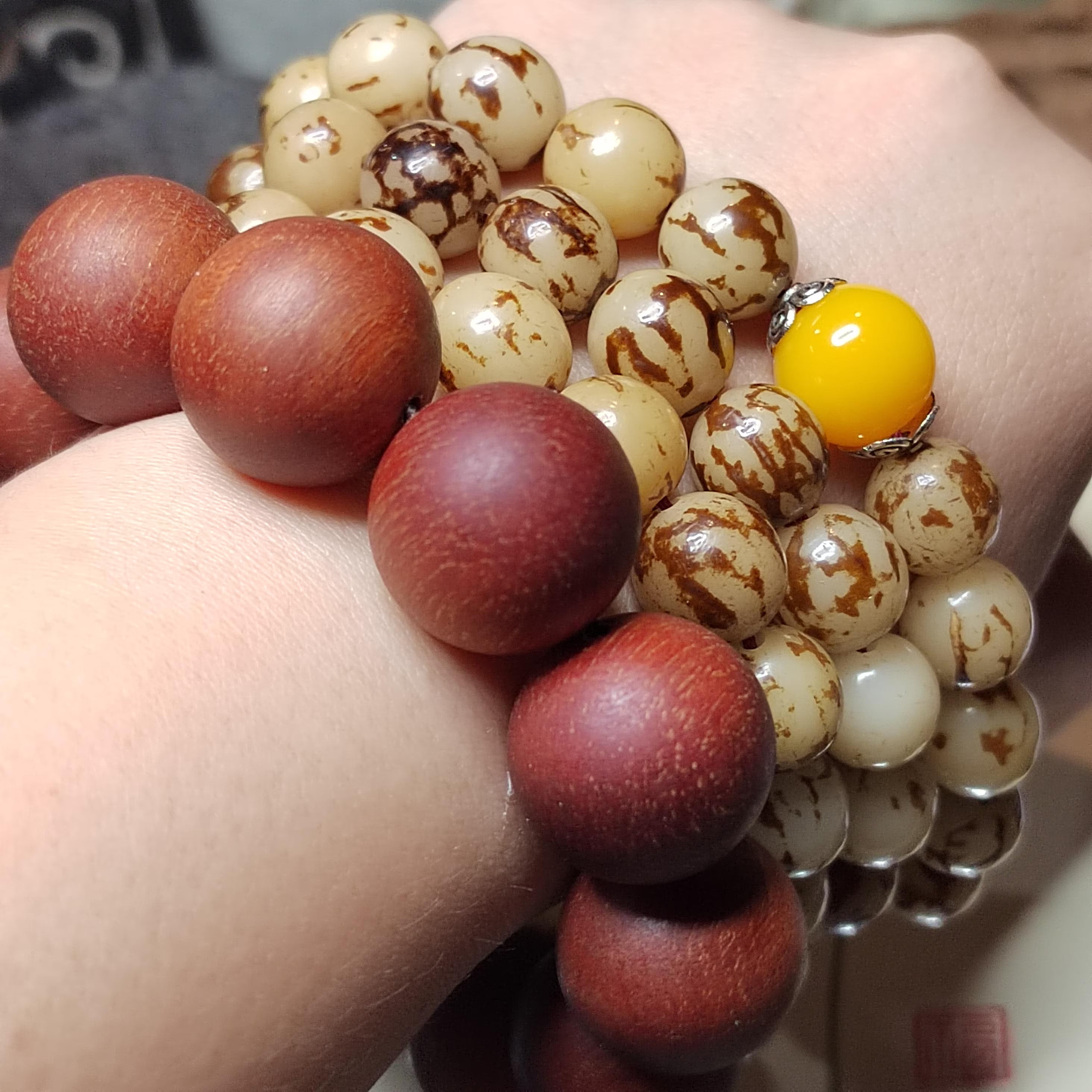 Close-up of a hand holding a bracelet with red, brown, and yellow beads.