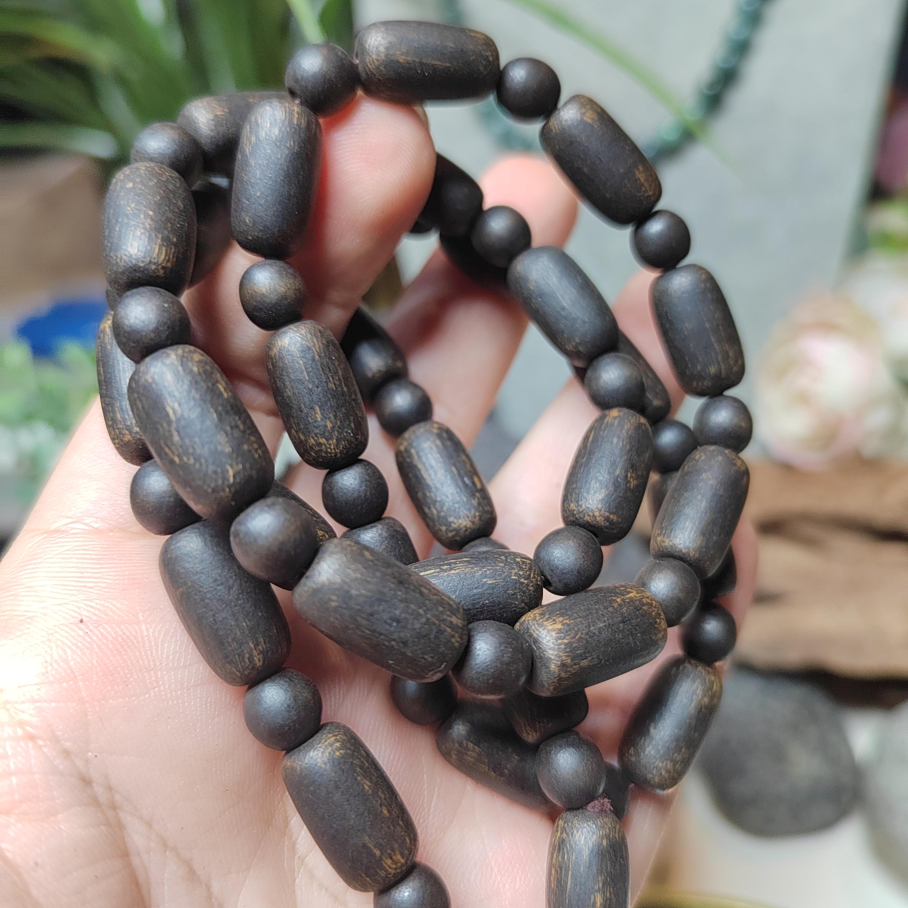 Dark wooden beaded necklace held in a hand with a blurred natural background