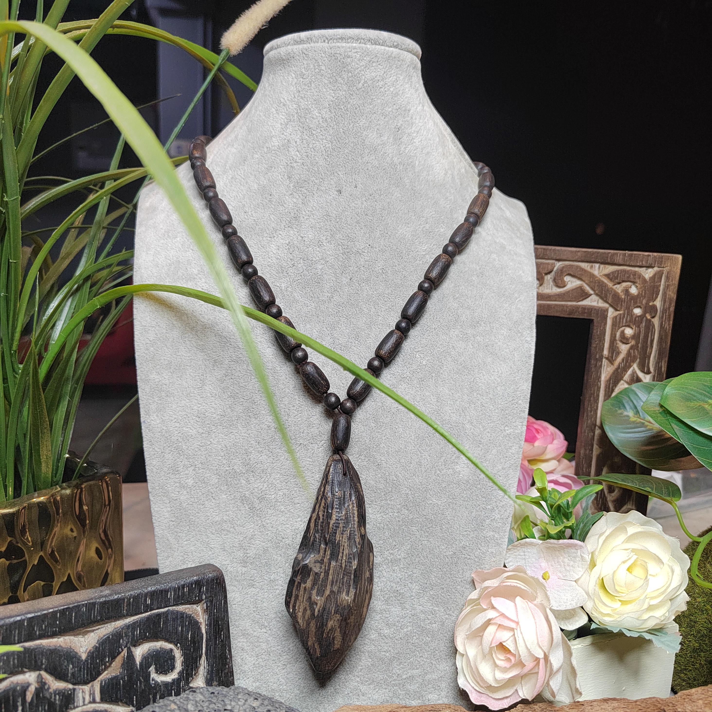 Necklace with dark beads and a large pendant on a gray stand with flowers and plants in the background