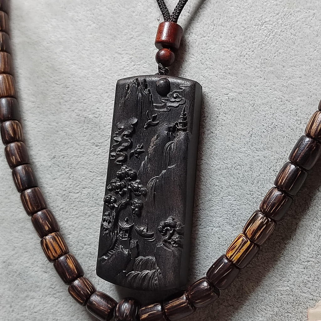 Necklace with a dark pendant featuring an engraved design on a light gray background
