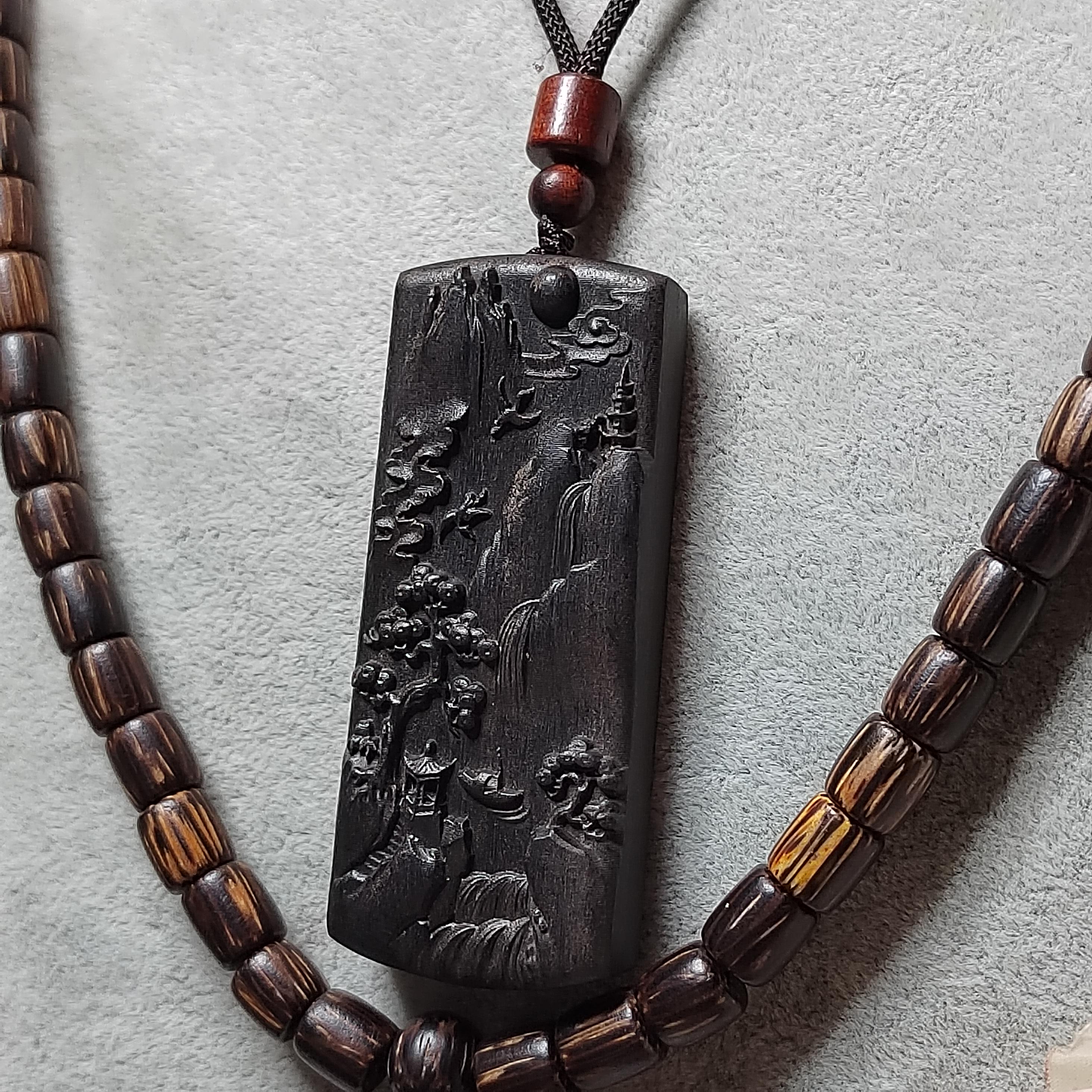 Necklace with a dark pendant featuring an engraved design on a light gray background