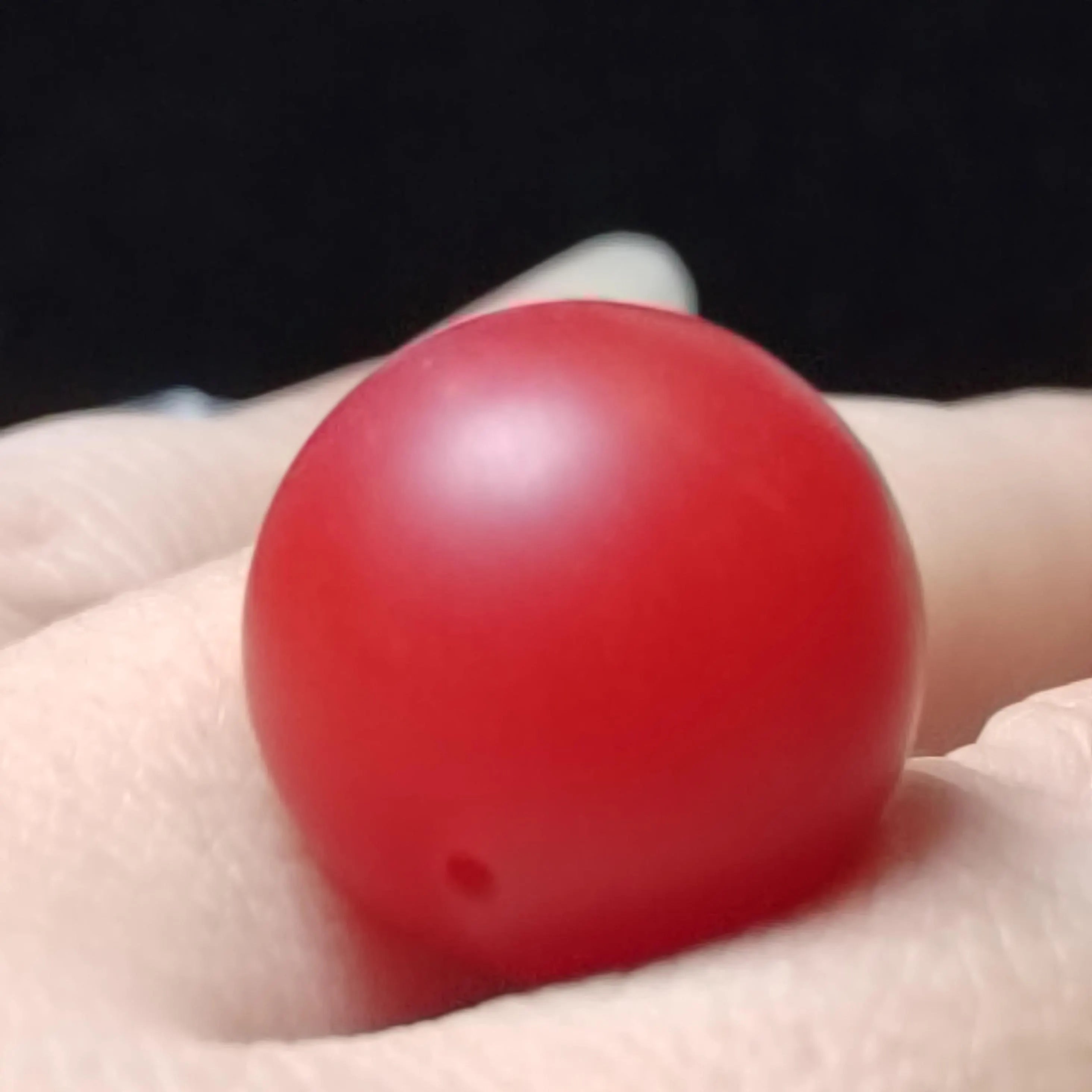 Red Nanhong bead held in a hand against a black background
