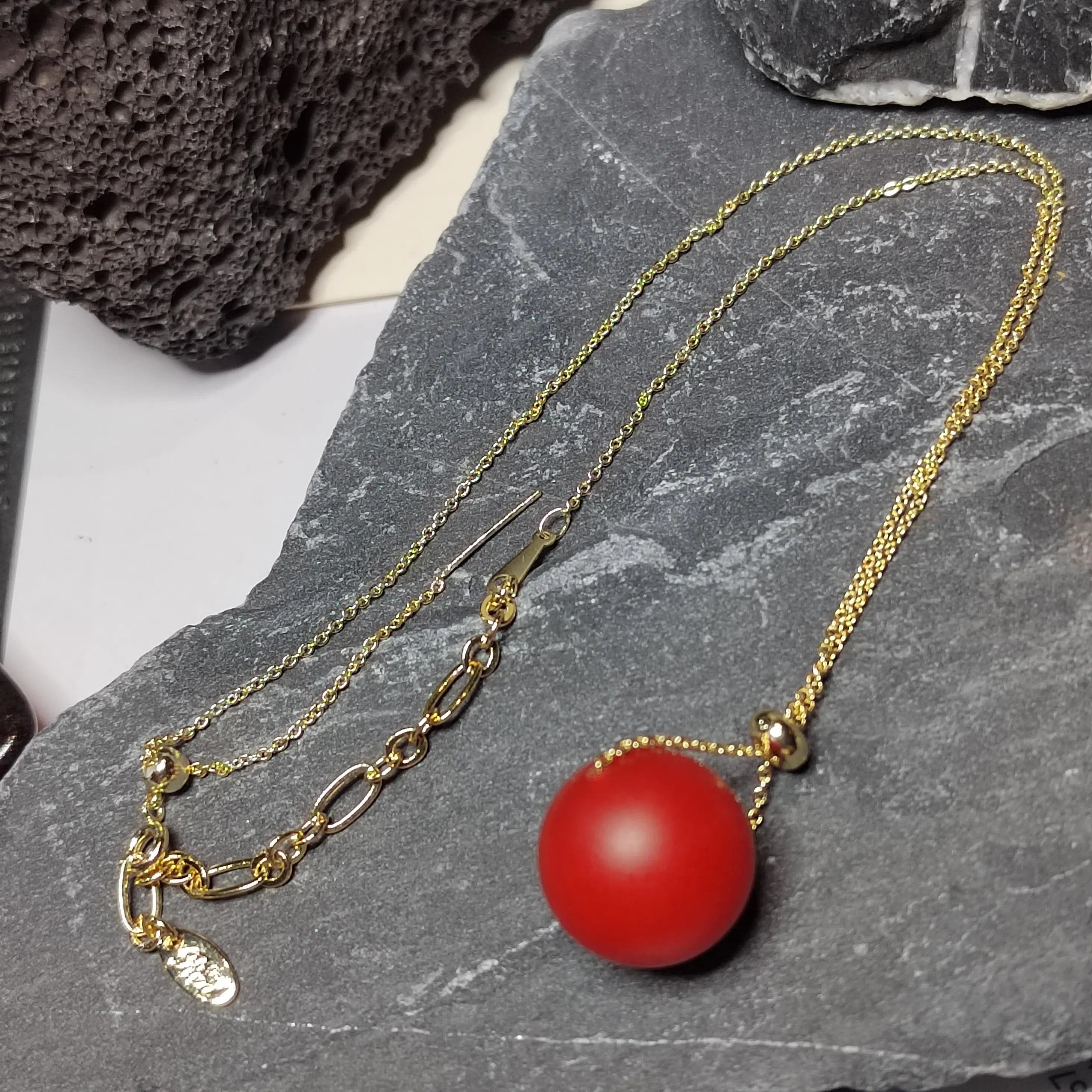 Gold necklace with a red Nanhong bead pendant on a stone surface