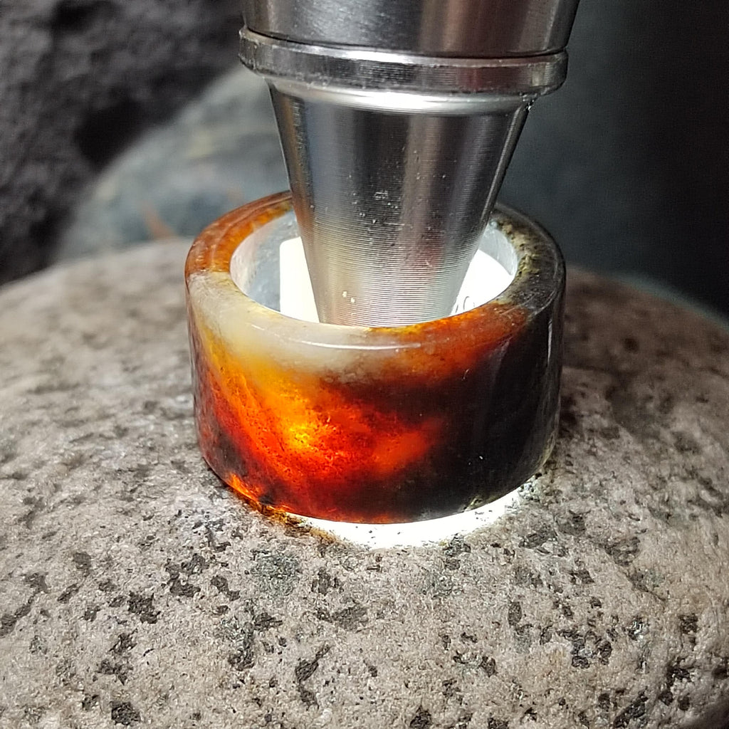 Close-up of a熔岩色玻璃环被金属工具压在岩石上