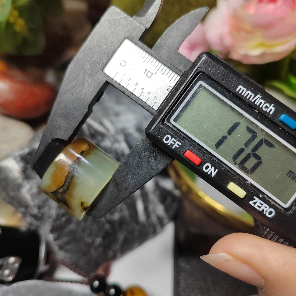 Digital caliper measuring a jade bead with a blurred natural background