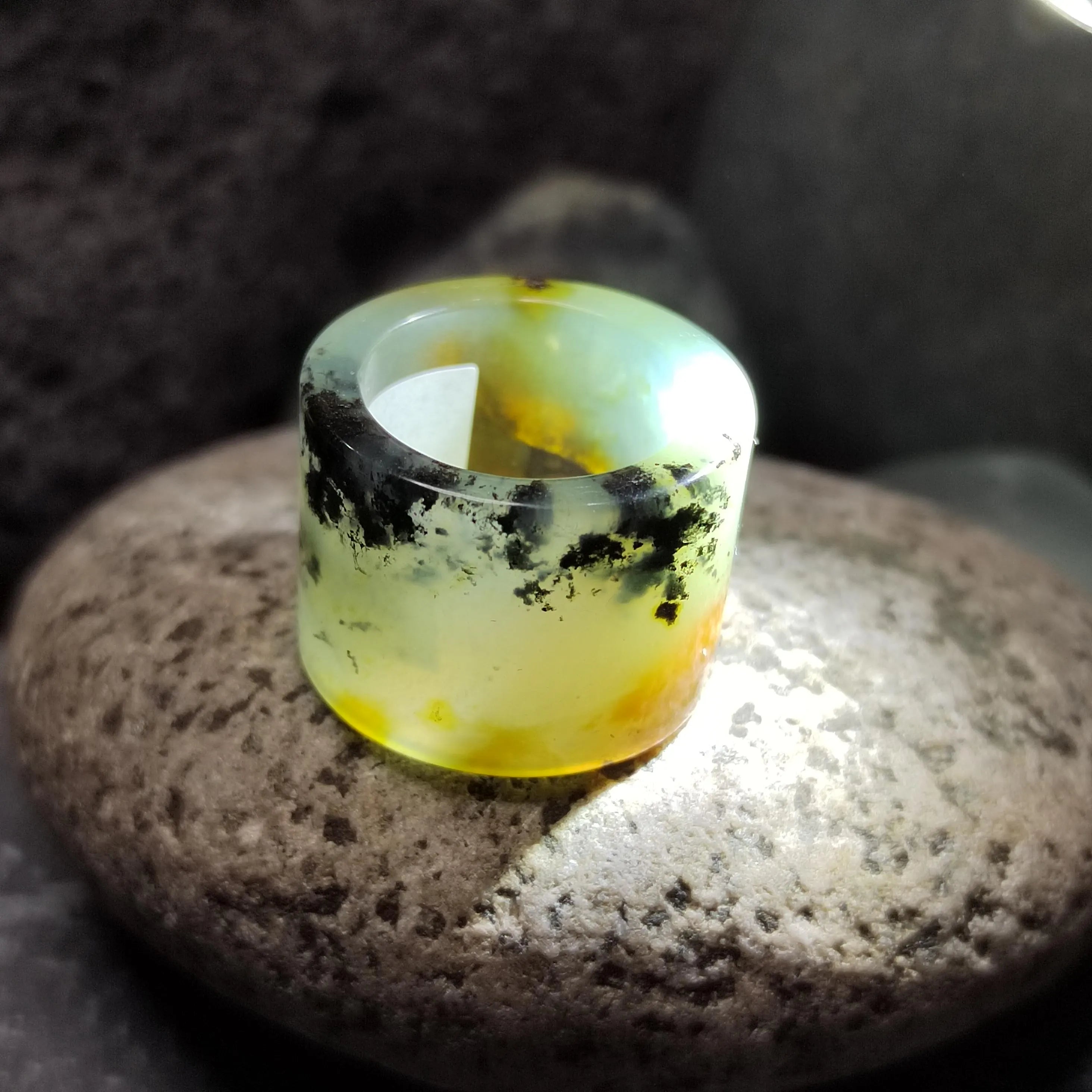 Translucent yellow ring with black inclusions on a dark stone surface