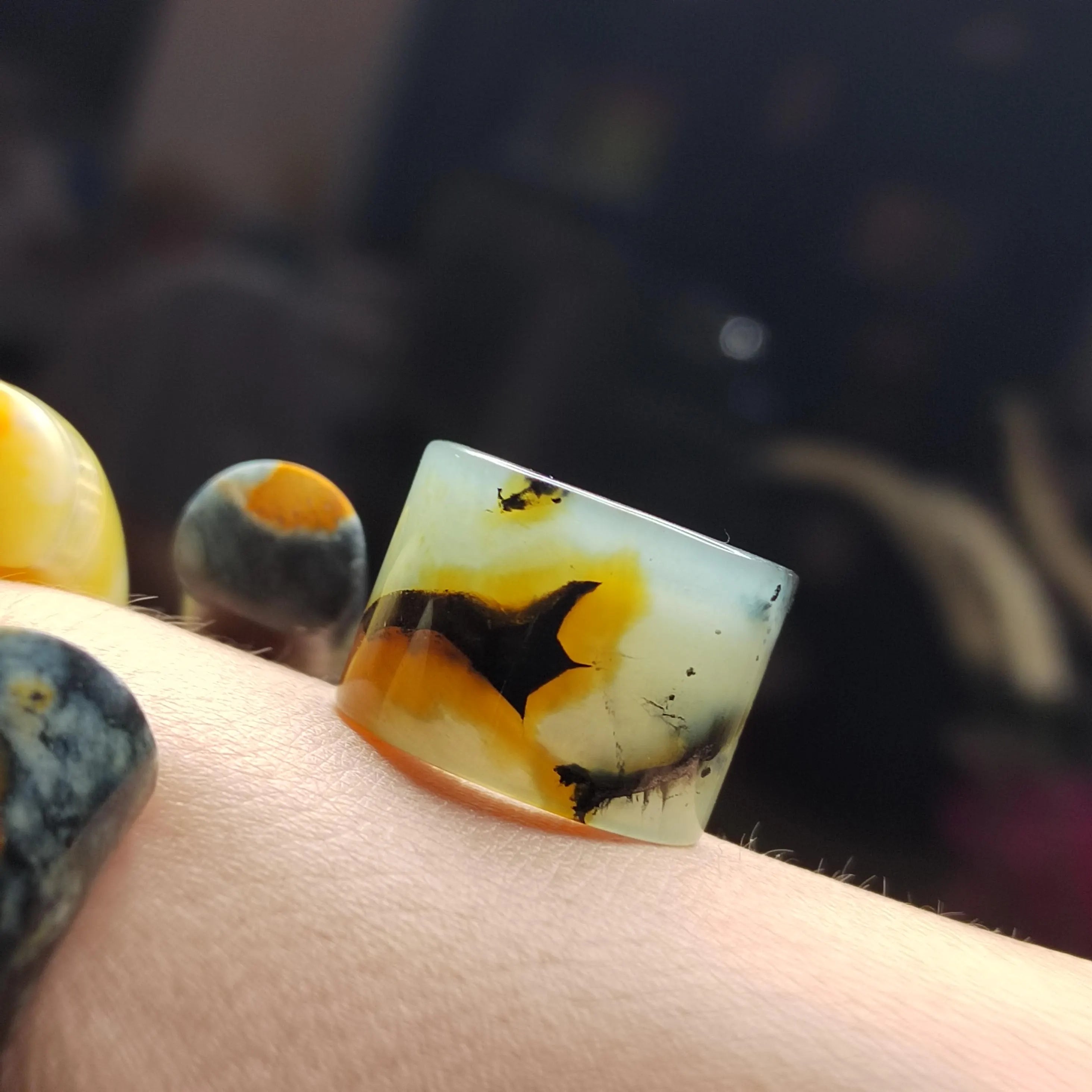 Close-up of a hand holding a rectangular stone with orange and black patterns against a blurred background