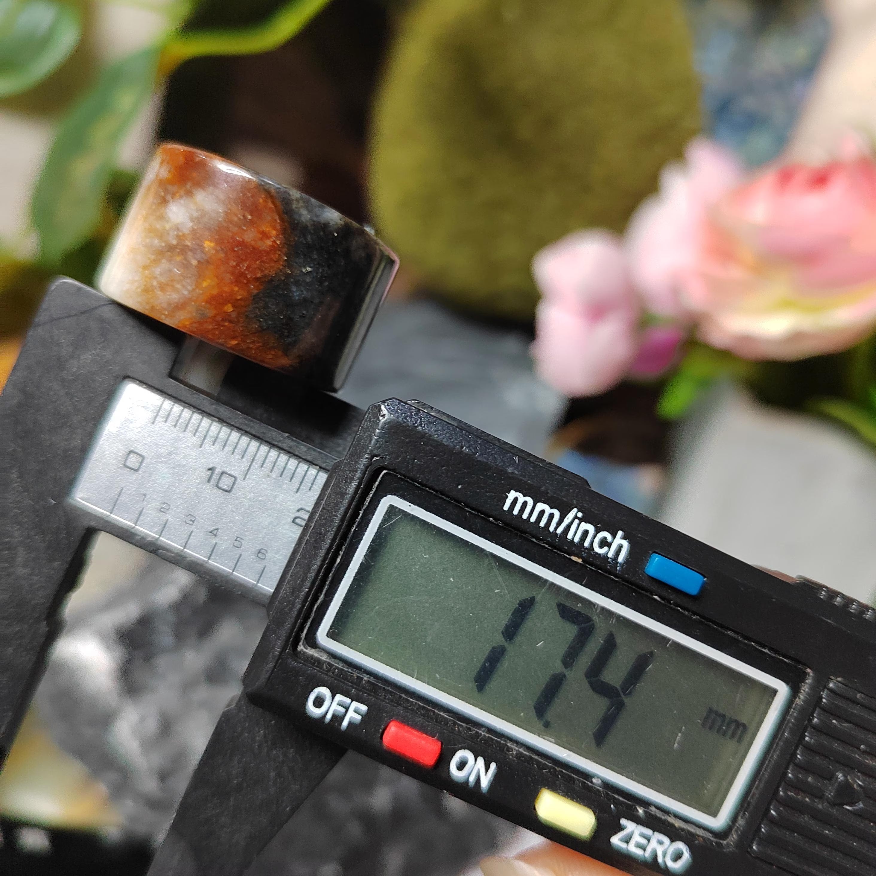 Digital caliper measuring a stone with a blurred natural background
