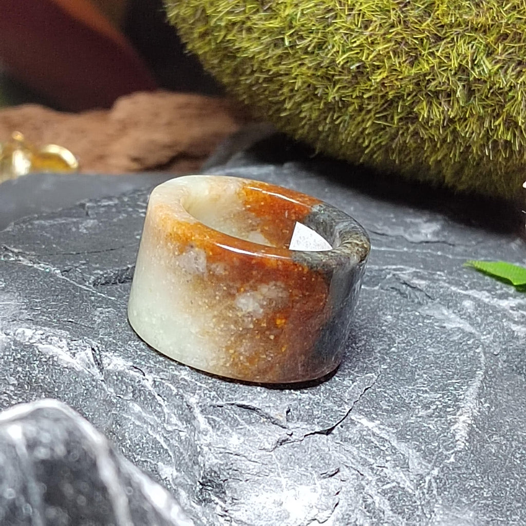 Brown and white stone ring on a textured surface with greenery in the background