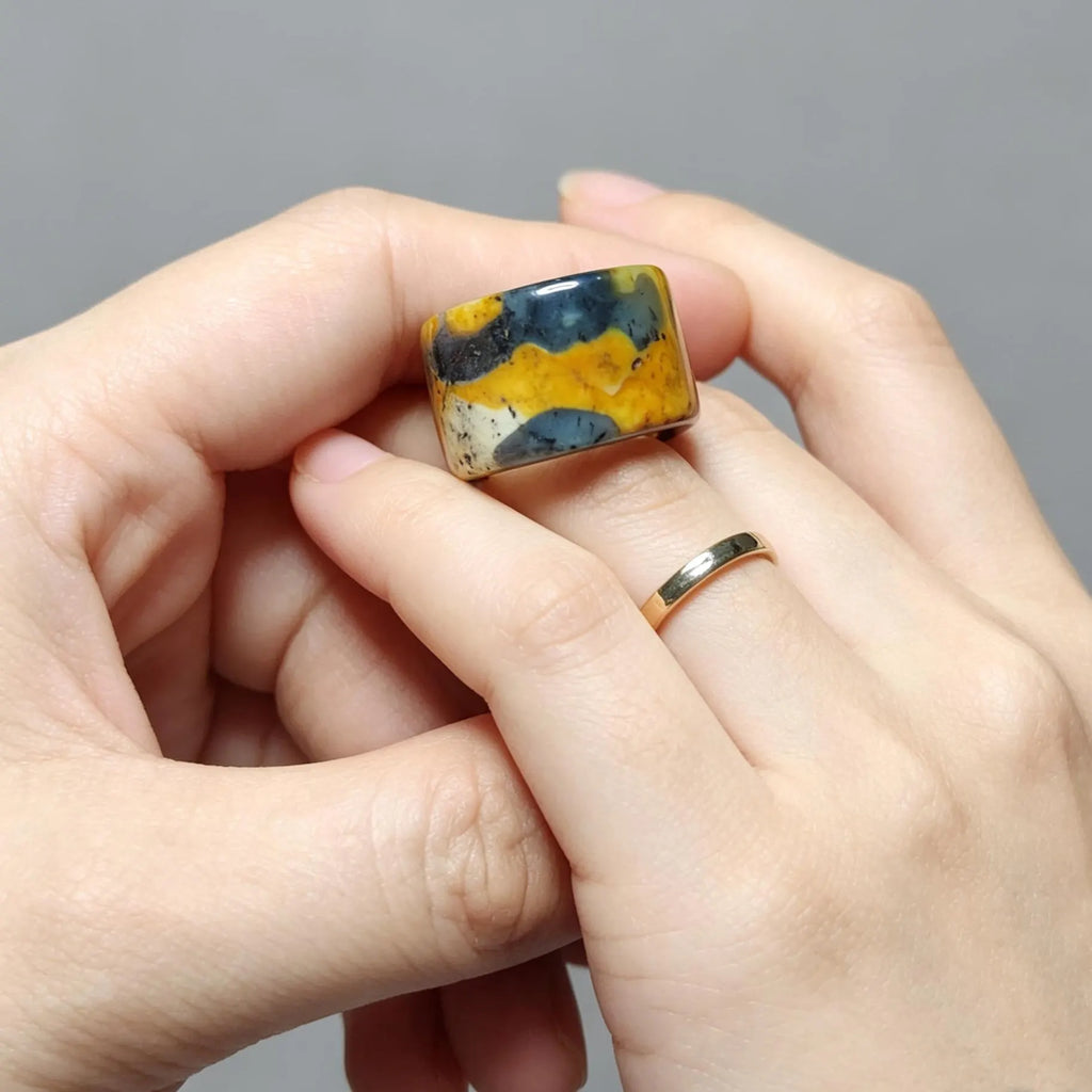 Hand holding a ring with a colorful stone against a gray background