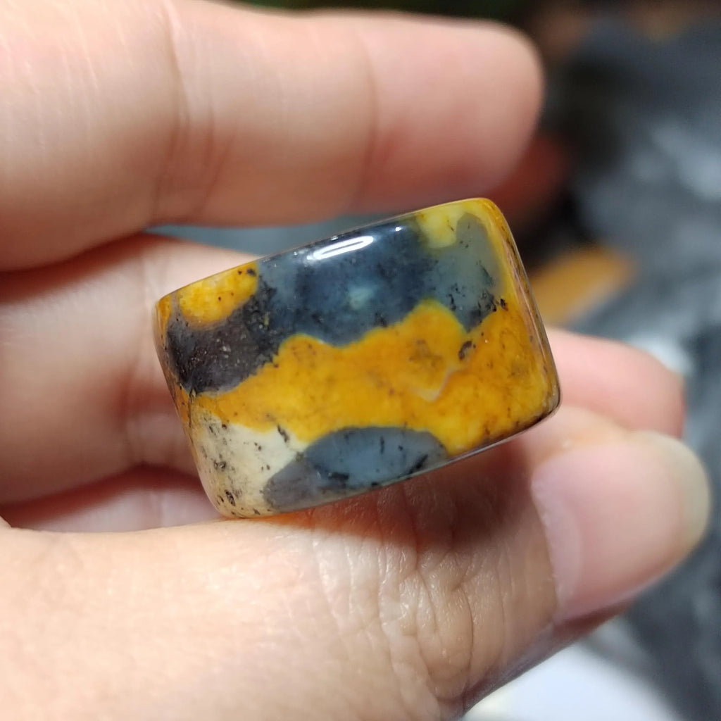 Hand holding a multicolored stone with yellow, blue, and white patterns.