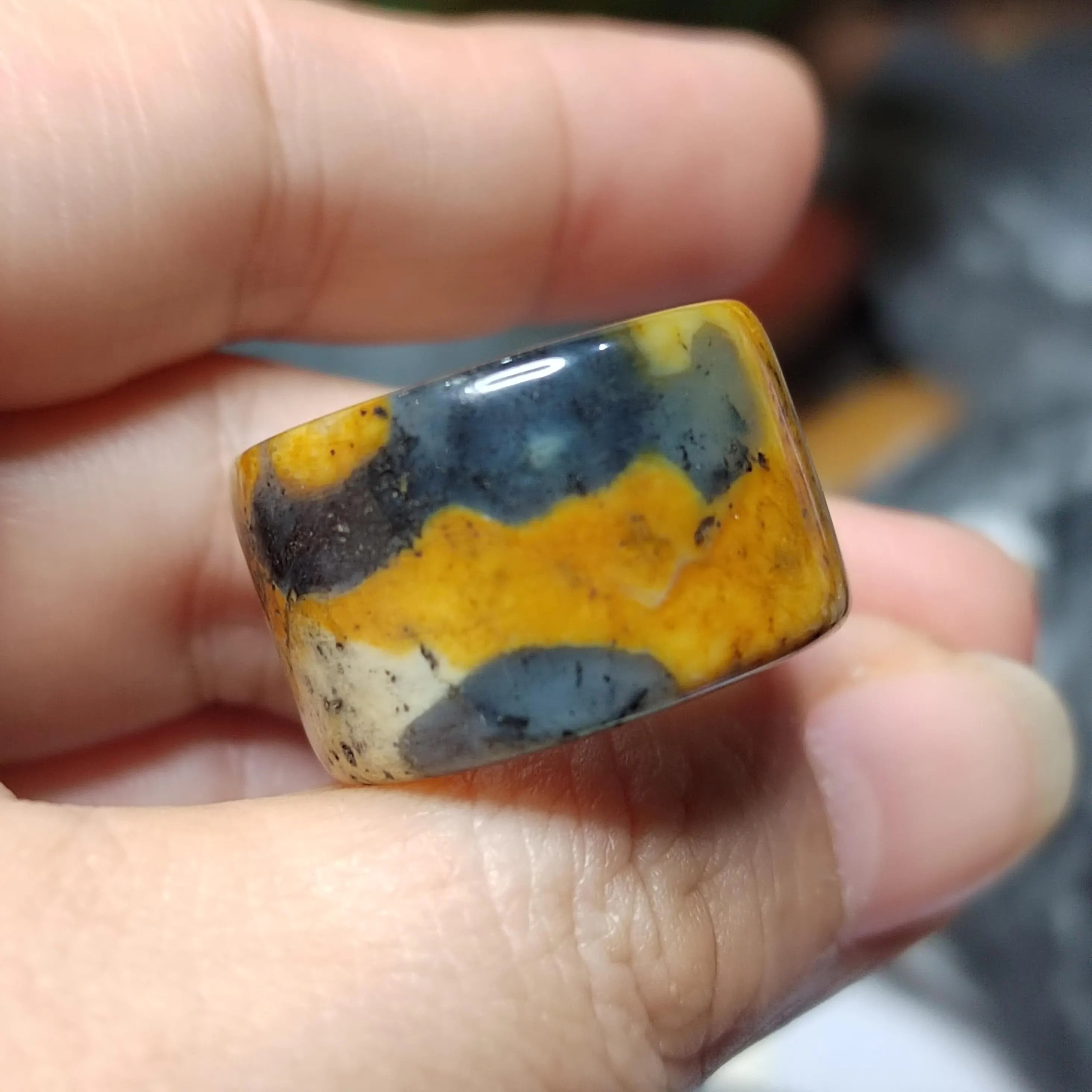 Hand holding a multicolored stone with yellow, blue, and white patterns.