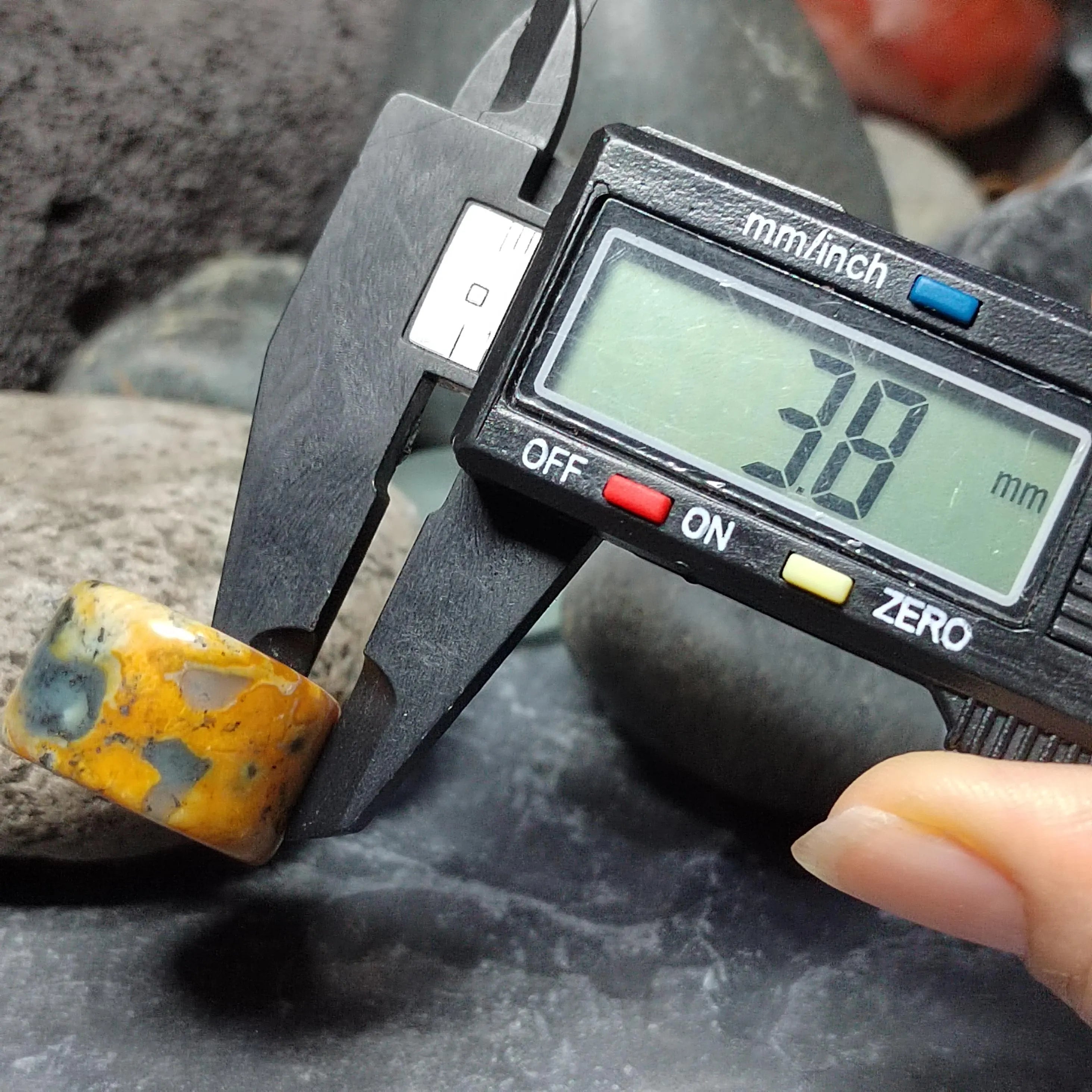Digital caliper measuring a yellowish-brown stone against a dark background