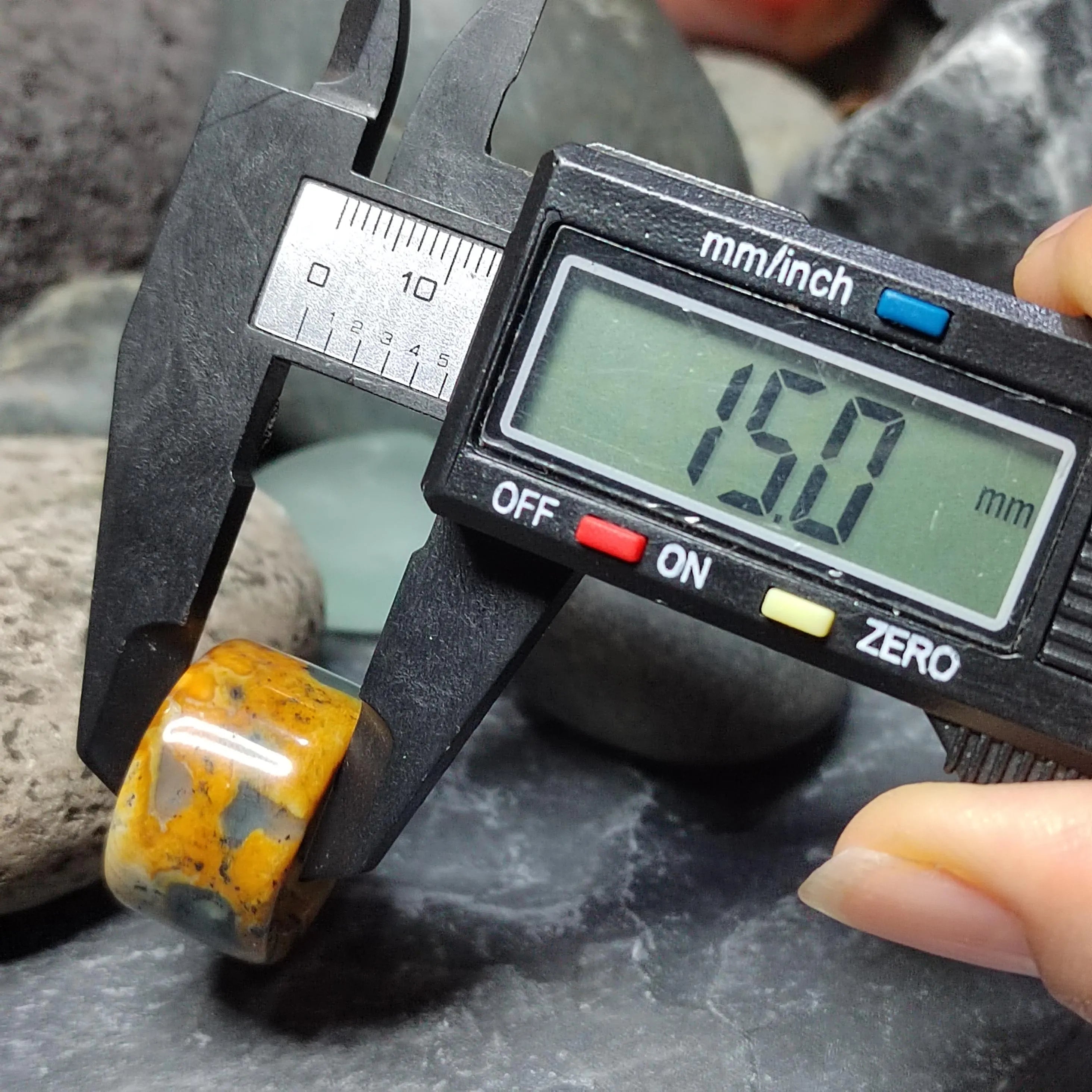 Digital caliper measuring a yellow stone against a rock background