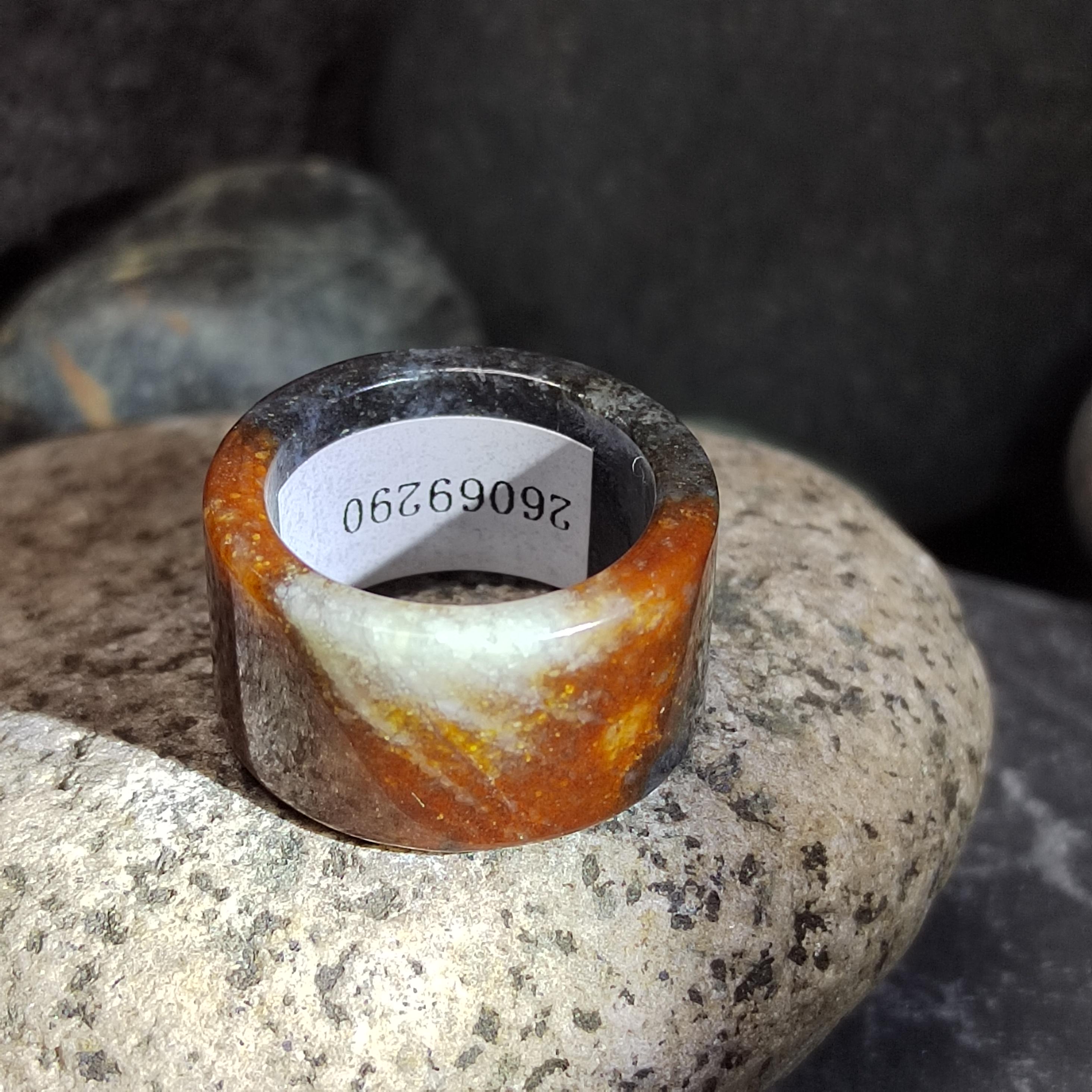 Ring with orange and white stone on a rock