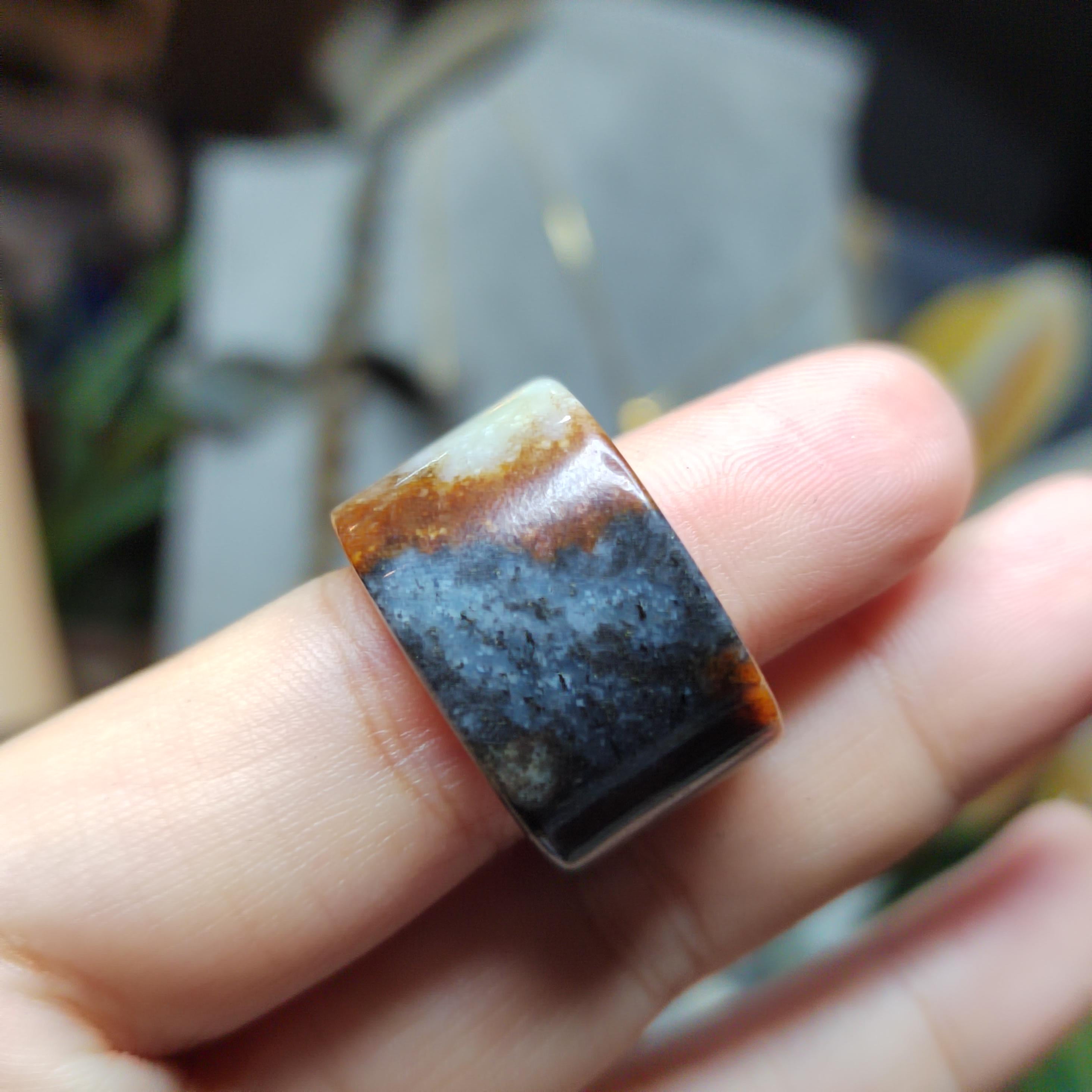 Hand holding a ring with a multicolored stone on a blurred background