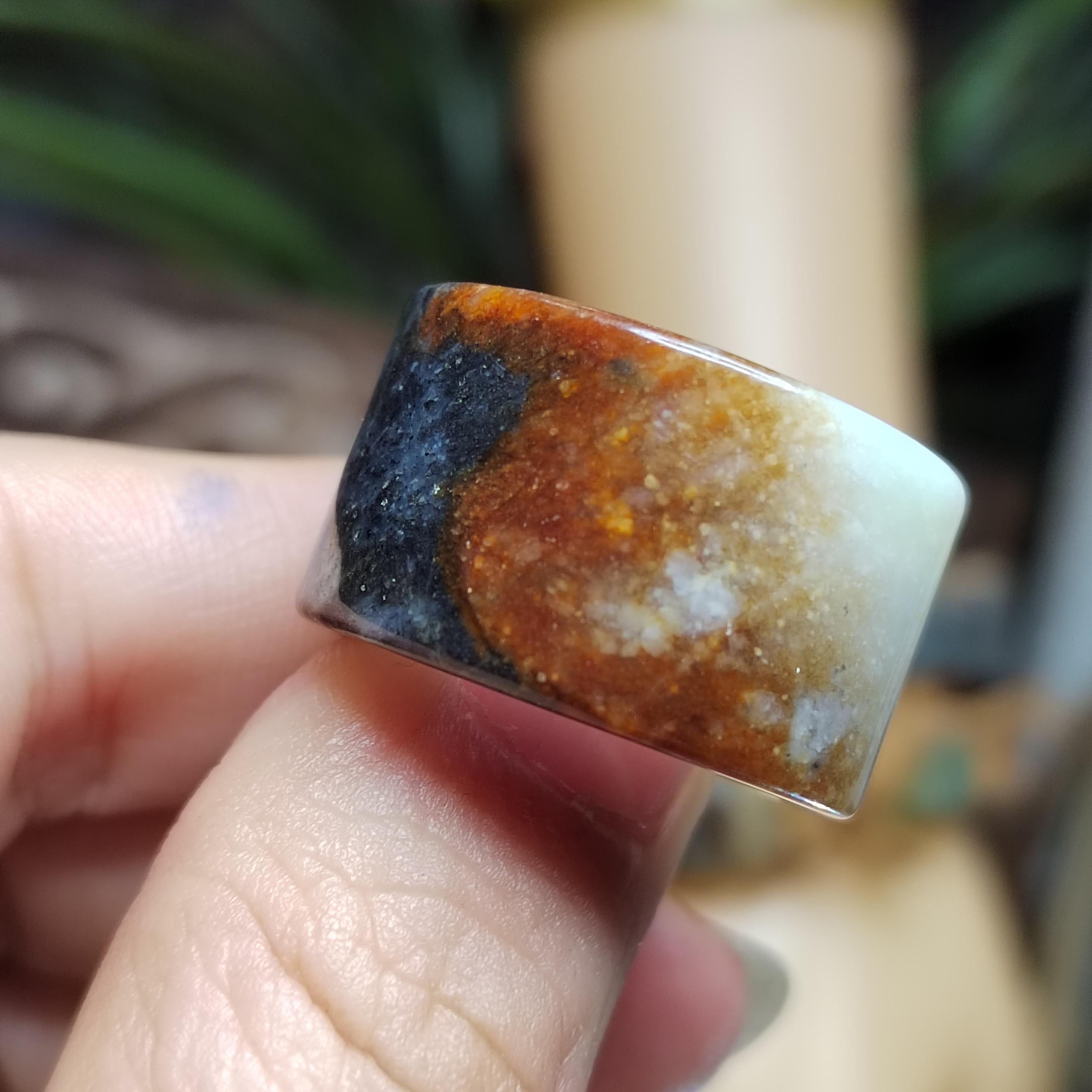Close-up of a hand holding a ring with a brown and black stone.