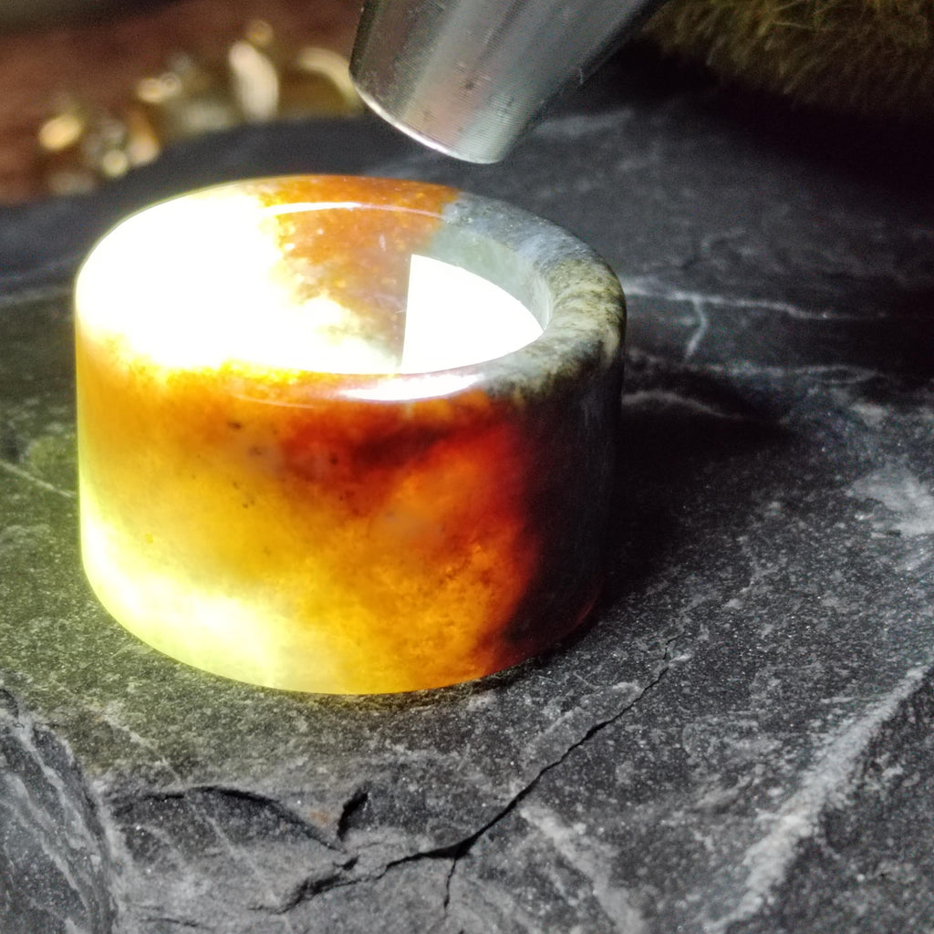 Close-up of a glowing amber-colored stone on a dark surface with a tool above it.