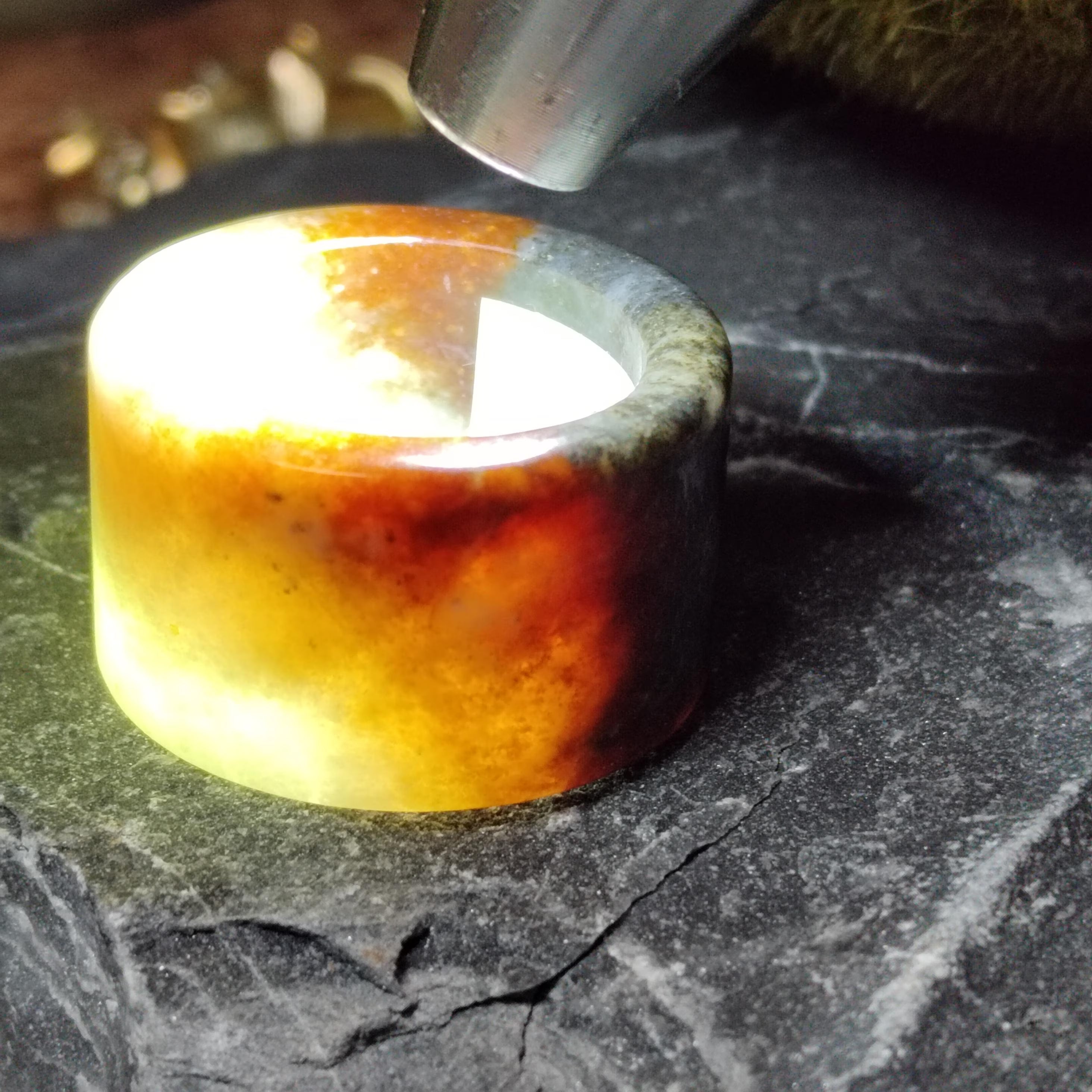 Close-up of a glowing amber-colored stone on a dark surface with a tool above it.
