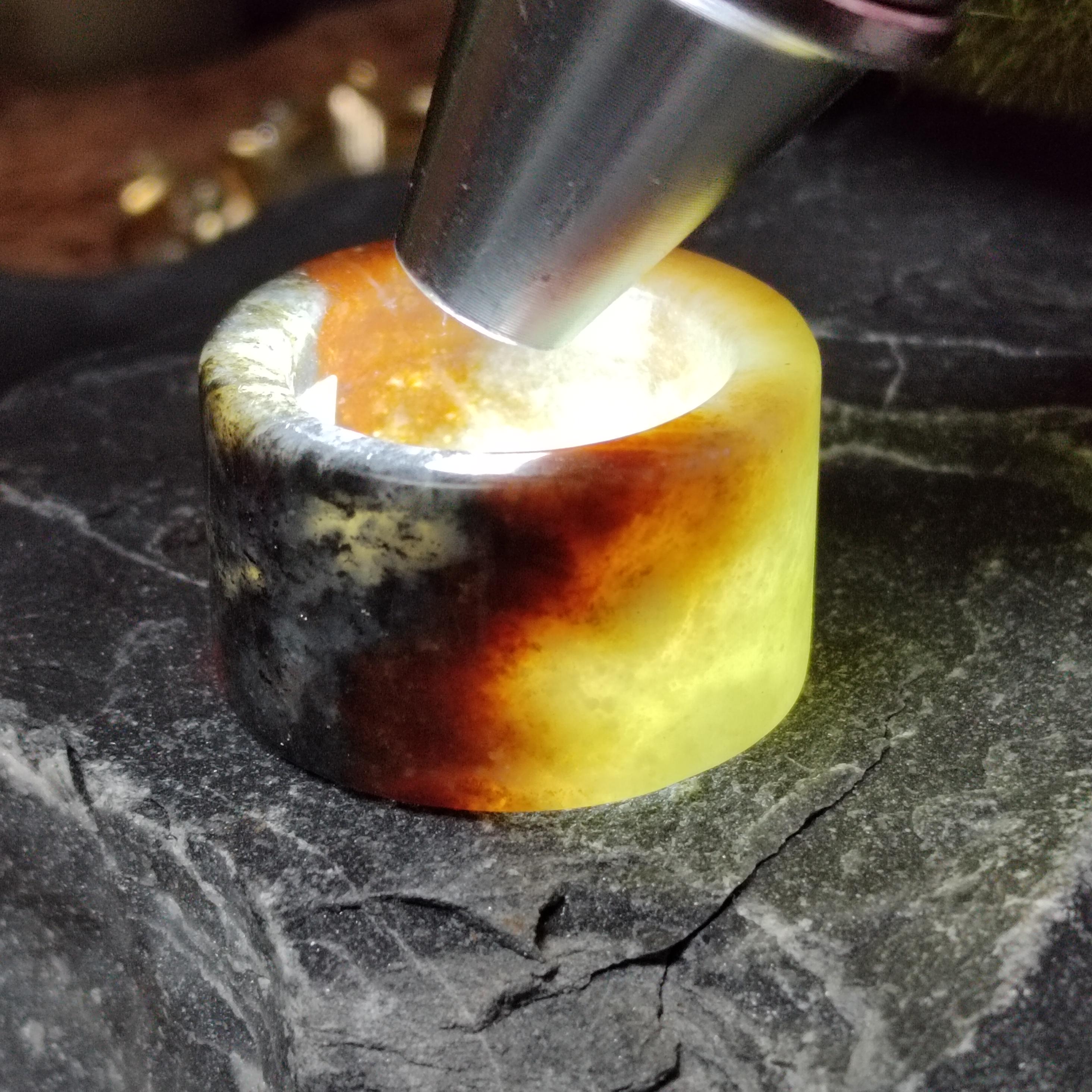 Close-up of a cylindrical amber stone being pressed with a metal tool on a dark surface.