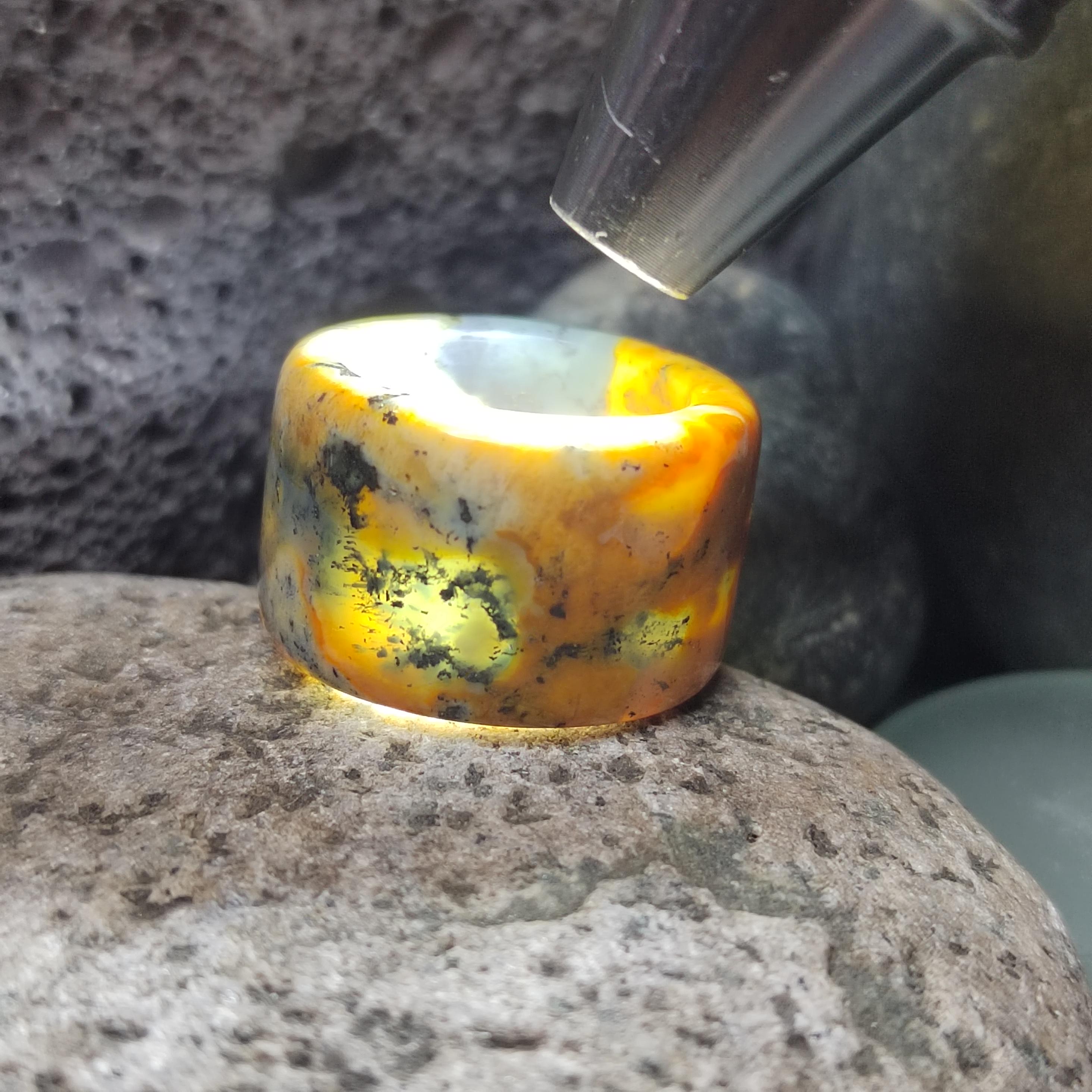 Polished bumblebee Jasper stone being examined with a magnifying glass on a rock surface.