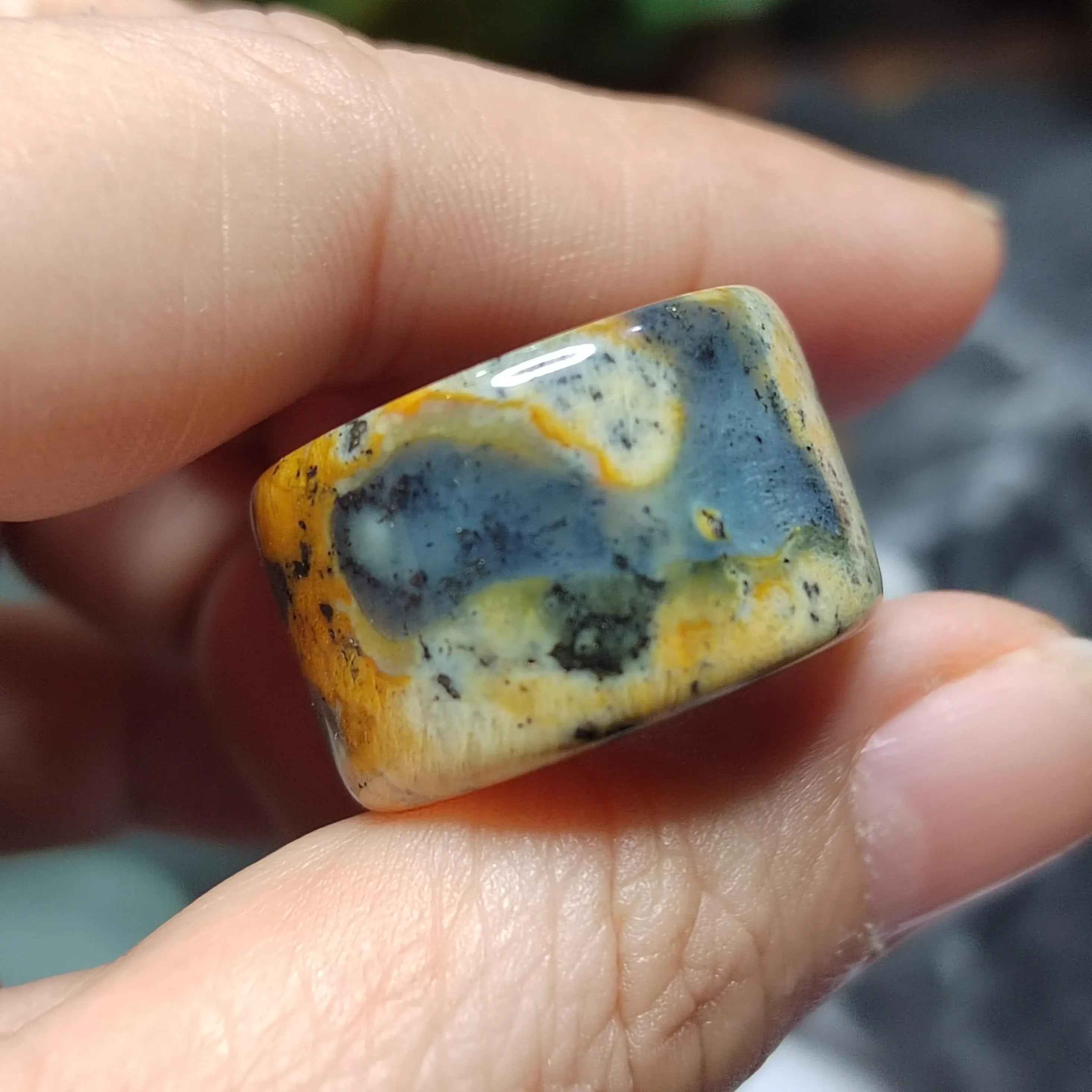 Hand holding a colorful stone with blue, yellow, and white patterns