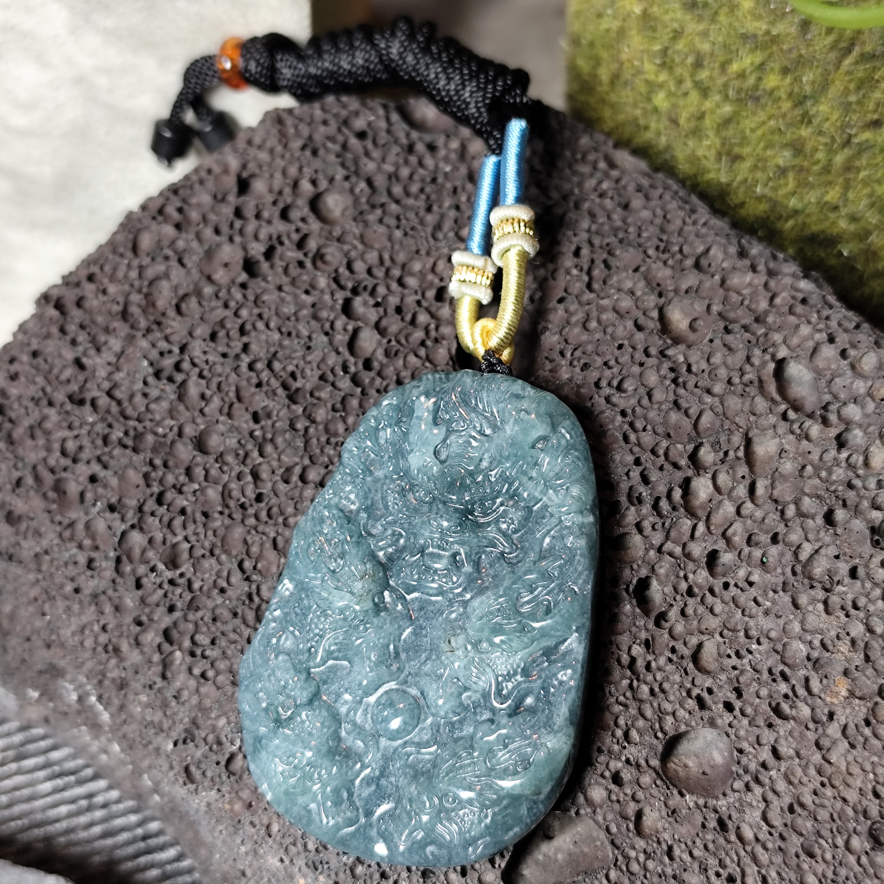Blue stone pendant on a black cord with a gold clasp, placed on a textured surface.